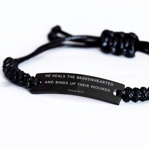 May include: Black braided bracelet with a black metal tag that reads "He heals the brokenhearted and binds up their wounds, Psalm 147:3".