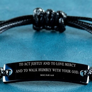 Puede incluir: Pulsera de cordón trenzado negro con una etiqueta de metal negro que dice "TO ACT JUSTLY AND TO LOVE MERCY AND TO WALK HUMBLY WITH YOUR GOD. MICAH 6:8"