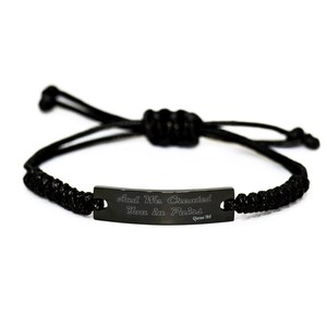 Puede incluir: Pulsera trenzada negra con una etiqueta de metal negro que dice "And We Created You in Pairs Quran 78:8".