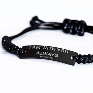 Puede incluir: Pulsera trenzada negra con una etiqueta de metal negro que dice "I AM WITH YOU ALWAYS MATTHEW 28:20".