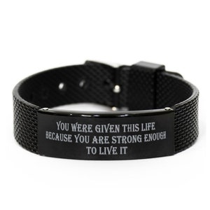 Pode incluir: Pulseira de silicone preta com uma placa de metal prateada gravada com a mensagem "You were given this life because you are strong enough to live it."