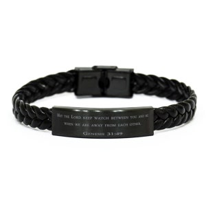 Puede incluir: Pulsera trenzada de cuero negro con una placa de metal plateado grabada con el texto "MAY THE LORD KEEP WATCH BETWEEN YOU AND ME WHEN WE ARE AWAY FROM EACH OTHER. GENESIS 31:49"