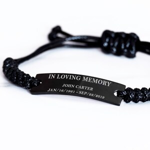 May include: Black braided bracelet with a black metal tag that reads "IN LOVING MEMORY JOHN CARTER JAN/16/1961 - SEP/22/2019".