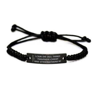 Puede incluir: Pulsera trenzada negra con una placa metálica rectangular. La placa presenta la inscripción "I CAN DO ALL THINGS THROUGH CHRIST WHO STRENGTHENS ME" y la referencia "PHILIPPIANS 4:13". La pulsera es ajustable.
