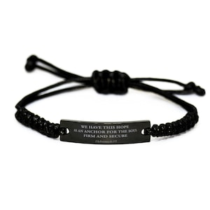 Puede incluir: Pulsera trenzada negra con una etiqueta de metal negro que dice "WE HAVE THIS HOPE AS AN ANCHOR FOR THE SOUL FIRM AND SECURE Hebrews 6:19".