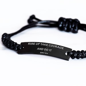 May include: Black braided bracelet with a black metal tag that reads "Rise Up Take Courage And Do It Ezra 10:4".