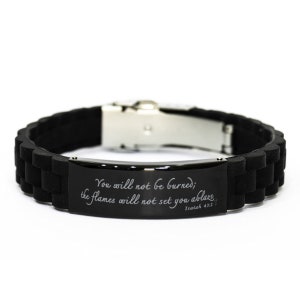 Pode incluir: Pulseira de silicone preta com fecho prateado e uma placa de metal preta gravada com o texto "You will not be burned; the flames will not set you ablaze Isaiah 43:2".