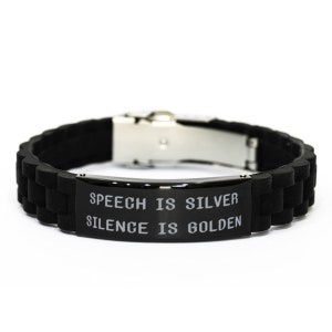 Puede incluir: Pulsera de silicona negra con cierre de metal plateado y una placa de metal negro con la inscripción "SPEECH IS SILVER SILENCE IS GOLDEN".