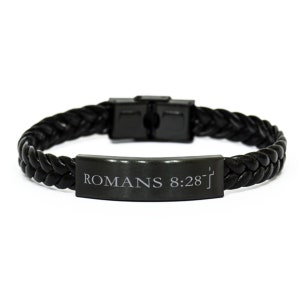 Puede incluir: Pulsera trenzada de cuero negro con una placa de metal negro grabada con el texto "ROMANS 8:28".
