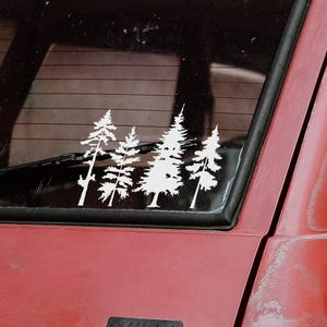 May include: A red car with a white pine tree decal on the rear window. The car has a roof rack and a black window frame. The decal is a silhouette of several trees.