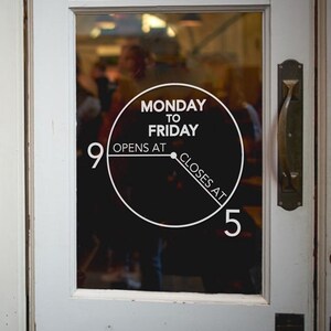 May include: A white sign on a glass door with black text that reads "Monday to Friday Opens at 9 Closes at 5".