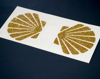 May include: Two gold glitter seashell stickers on a white background.