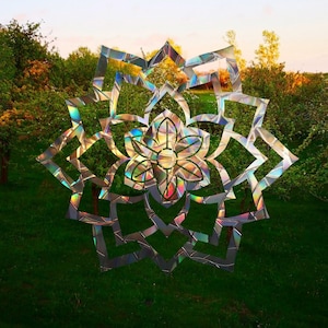 Könnte beinhalten: Ein farbenfrohes, schillerndes Mandala-Design mit einer Blume in der Mitte, vor dem Hintergrund grüner Bäume und blauen Himmels.