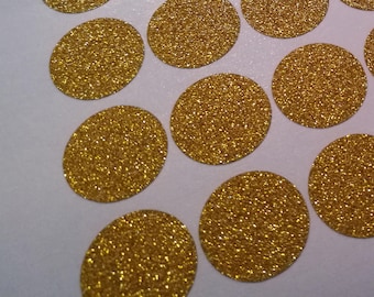 May include: A sheet of gold glitter circle stickers. The stickers are arranged in rows and columns on a white background. The glitter is a bright, shiny gold colour. The stickers are round and have a slightly textured surface.