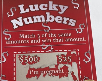 May include: A red and white scratch-off lottery ticket with the text "Lucky Numbers" and "Match 3 of the same amounts and win that amount." The ticket has three scratch-off areas with the amounts $500, $25, and "I'm pregnant".