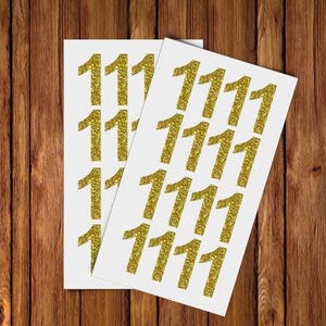 May include: Two sheets of white paper with gold glitter numbers 1111 printed on them. The numbers are arranged in rows and columns.