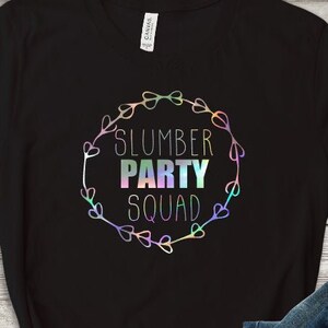 May include: Black v-neck t-shirt with a rainbow iridescent graphic that says "Slumber Party Squad" in a circle with hearts.