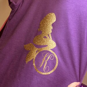 May include: Purple t-shirt with a gold glitter mermaid silhouette and a gold glitter monogram "H" in a circle.