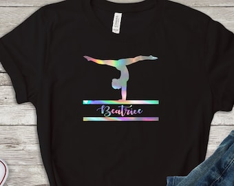 May include: Black t-shirt with a holographic image of a gymnast performing a handstand on a balance beam. The name "Beatrice" is printed below the image.