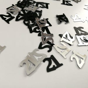 以下が含まれることがあります： 黒と銀のコンフェッティで、それぞれに数字の21が印刷されています。