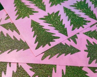 May include: A stack of pink paper cutouts of green glitter Christmas trees.