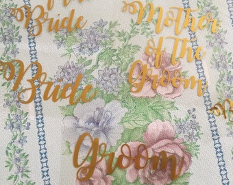 May include: Gold glitter wedding table place cards with the text "Mother of the Bride", "Bride", "Mother of the Groom", "Groom", "Flower Girl", and "Bridesmaid".