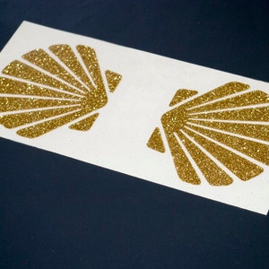 May include: Two gold glitter seashell stickers on a white background.