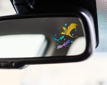 May include: A rearview mirror with a holographic sticker of a group of dragons flying in a starry sky. The dragons are iridescent with shades of blue, green, and yellow.