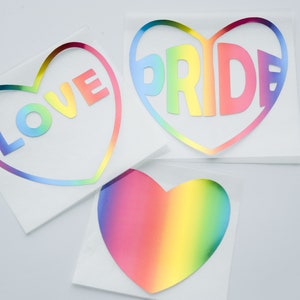 Pode incluir: Três adesivos em forma de coração arco-íris com as palavras "LOVE" e "PRIDE" neles.