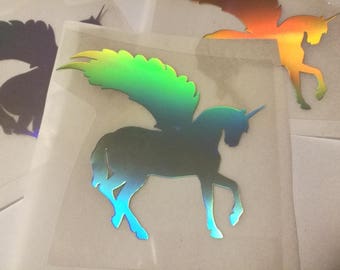 May include: A holographic iridescent sticker of a unicorn with wings. The unicorn is facing right and has a horn on its head. The wings are spread out behind the unicorn.