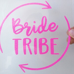 Op de afbeelding: Roze glitter vinyl sticker met de tekst "Bride Tribe" in een cirkel met pijlen.