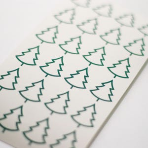Op de afbeelding: Een vel witte stickers met een herhaald patroon van groene kerstboomcontouren. De bomen zijn eenvoudig, gestileerd en gelijkmatig verdeeld. Perfect voor knutselen of decoraties tijdens de feestdagen.