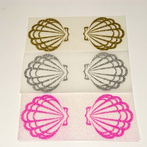Könnte beinhalten: Drei Sätze glitzernder Bügelbilder in Form von Muscheln. Der erste Satz ist golden, der zweite silbern und der dritte rosa.
