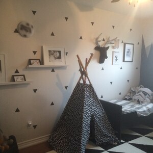 Può includere: Una tenda a forma di tipi bianca e nera con un tessuto a motivi bianchi e neri. Il tipi è allestito in una stanza con una parete bianca decorata con adesivi triangolari neri. C'è un tappeto a motivi bianchi e neri sul pavimento. La stanza ha anche un letto nero con un copriletto a righe bianche e grigie e un cuscino bianco con una grafica bianca e nera. C'è un quadro incorniciato sul muro con il testo "Boys Rule".