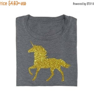 May include: A gray t-shirt with a gold glitter unicorn design.