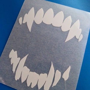 May include: White vinyl sticker with two sets of teeth, one set is larger and the other is smaller. The teeth are in the shape of a mouth.
