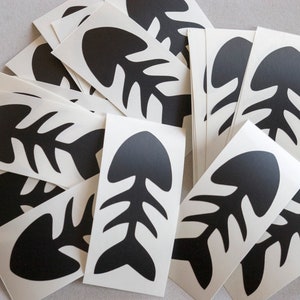 Op de afbeelding: Een stapel witte stickers met zwarte visgraatontwerpen. De visgraten zijn gestileerd en hebben een eenvoudige, moderne uitstraling.