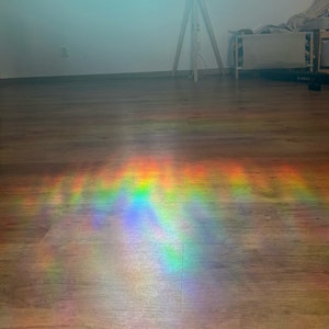 May include: A rainbow prism effect is cast on a wooden floor, creating a colourful and abstract pattern of light.