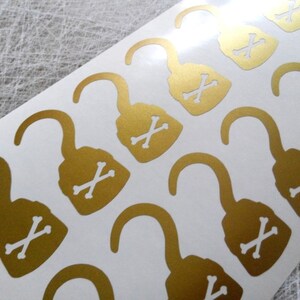 May include: A sheet of gold-colored stickers with a pirate hook and crossbones design. The stickers are on a white background.