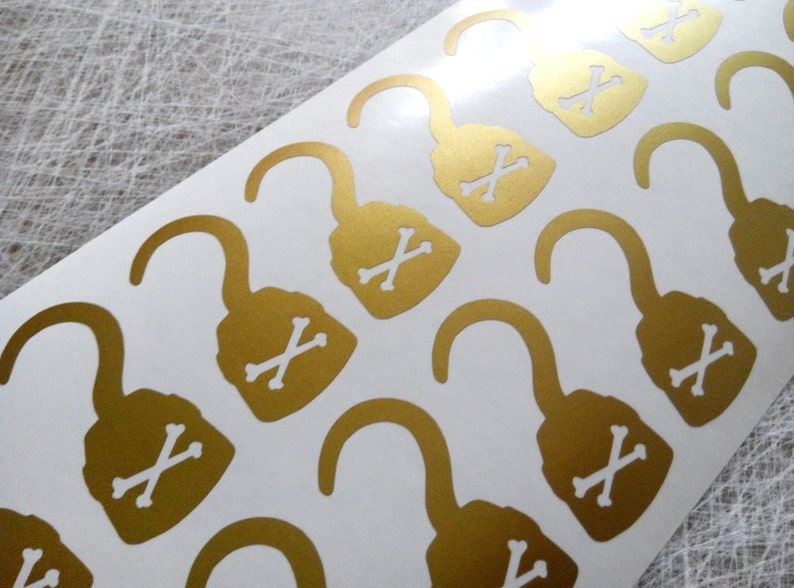 May include: A sheet of gold-colored stickers with a pirate hook and crossbones design. The stickers are on a white background.
