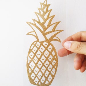 May include: Gold glitter pineapple decal on a clear background. The pineapple is outlined in black and has a detailed design.