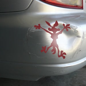May include: A silver car bumper with a red cartoon coyote sticker. The bumper has several scratches and dents.