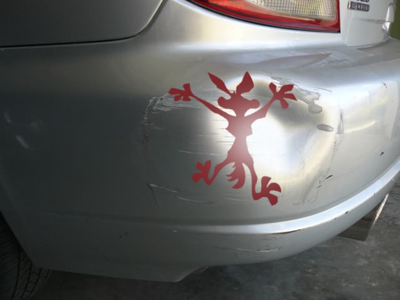 May include: A silver car bumper with a red cartoon coyote sticker. The bumper has several scratches and dents.