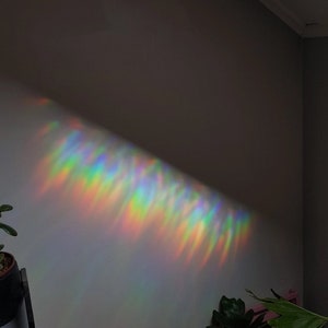 May include: A rainbow prism light refracts through a window, casting a colourful, shimmering pattern on a white wall.