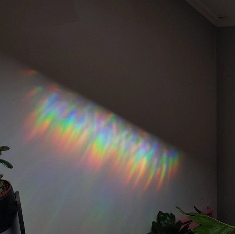 May include: A rainbow prism light refracts through a window, casting a colourful, shimmering pattern on a white wall.