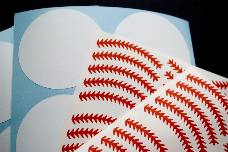 May include: A sheet of white circle stickers with red baseball stitching designs. The stickers are on a light blue background.