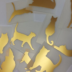 Peut inclure: Un ensemble de dix autocollants de silhouette de chat dorés. Les autocollants sont sur un fond blanc.