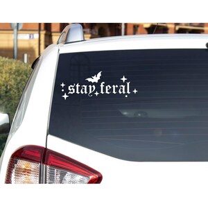 May include: White vinyl car sticker with a bat and the text "stay feral" in a gothic font.