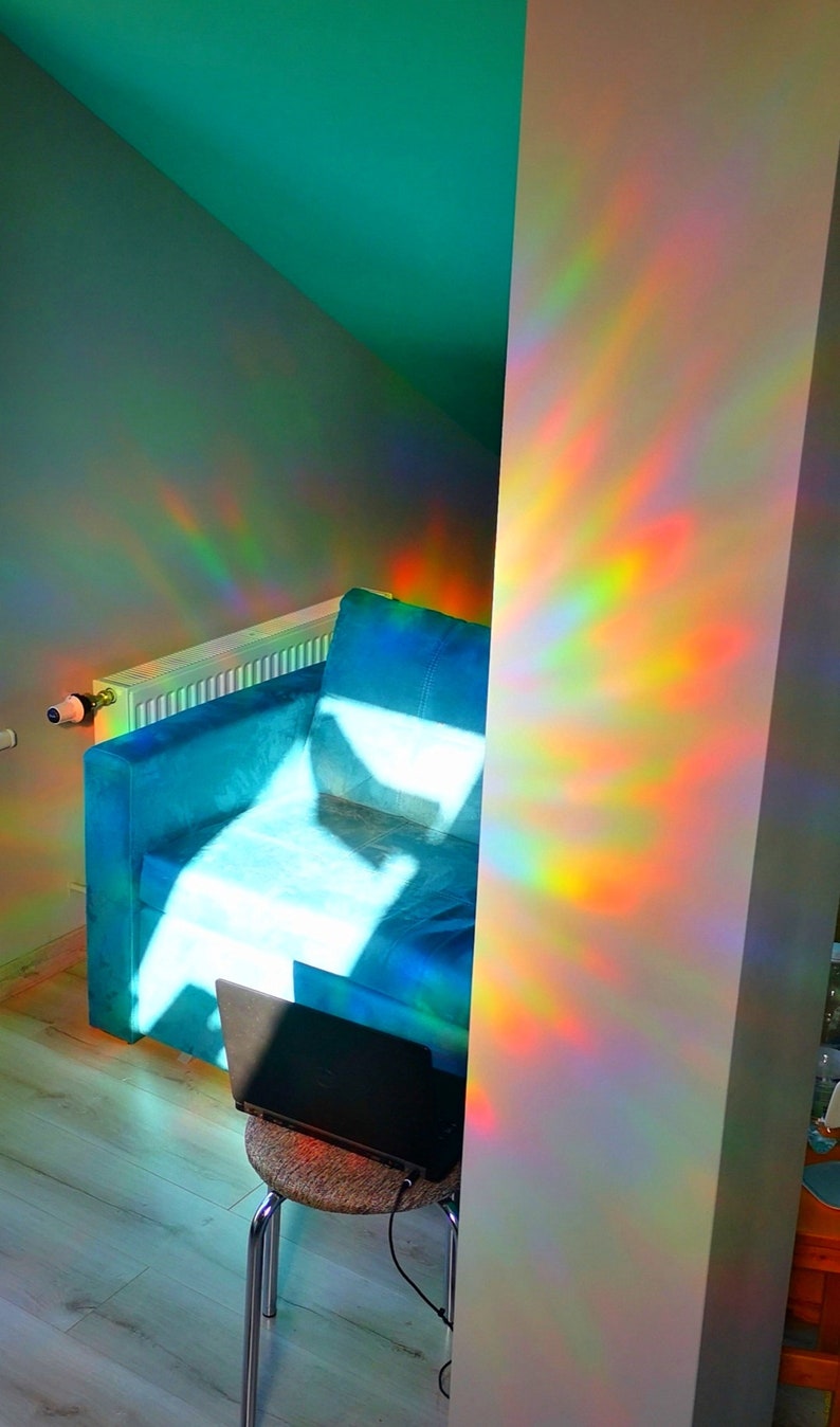 May include: A blue sofa with a laptop on a small stool in a room with a green wall and a white wall with rainbow light reflections.