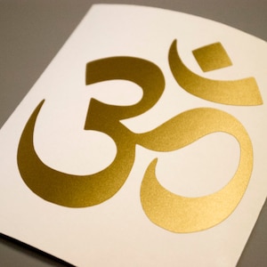 May include: Gold Om symbol sticker on a white background.